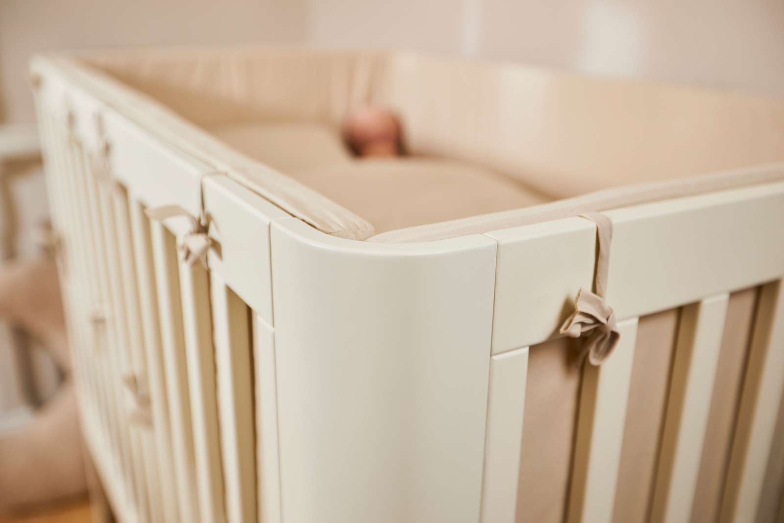 FLEXA baby bed, 140x70 cm, cream finish, visible soft padding, child resting inside; nursery context.
