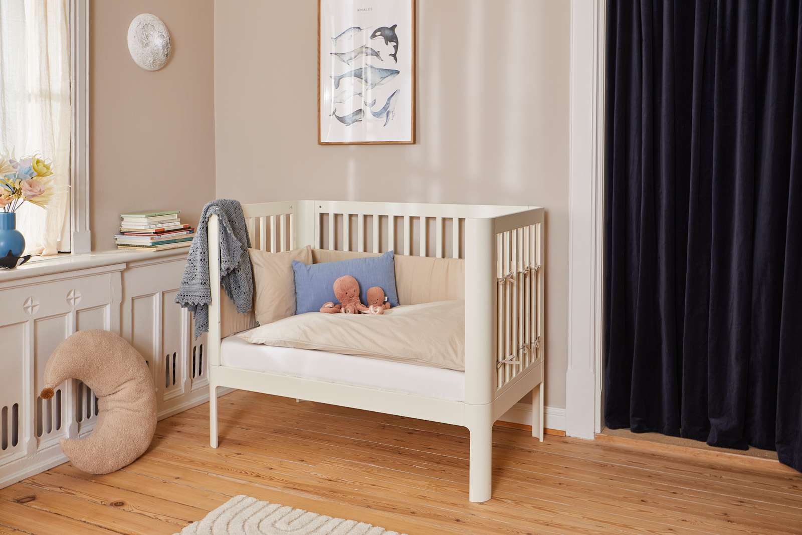 Cream FLEXA Baby Bed, 140x70cm, wood, with pillows and toys in a softly lit nursery with child-safe rounded edges.