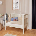 Cream FLEXA Baby Bed, 140x70cm, wood, with pillows and toys in a softly lit nursery with child-safe rounded edges.