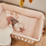 Woman beside FLEXA baby bed from OAK collection, light wood finish, in nursery with child-safe rounded edges visible.