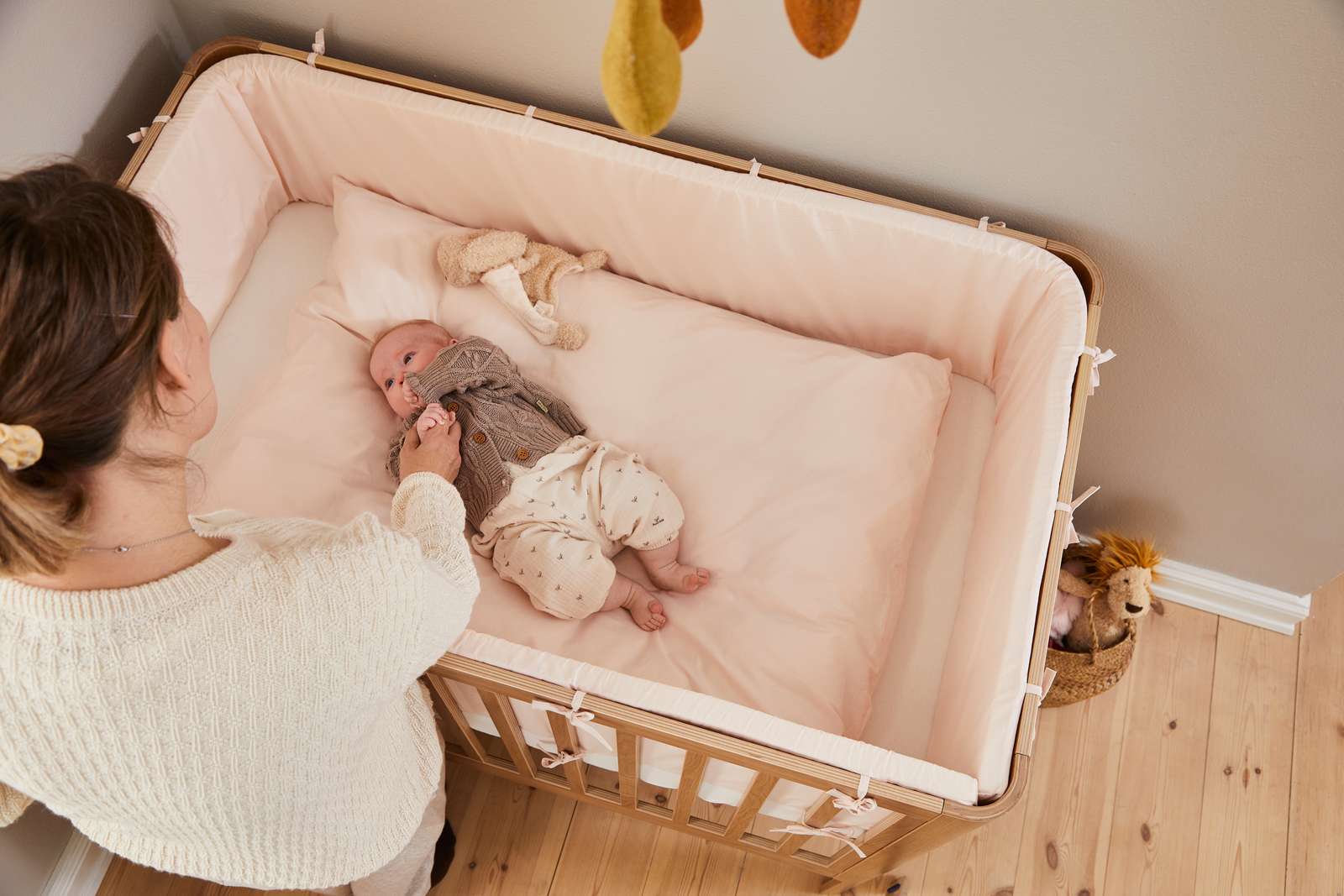 Woman beside FLEXA baby bed from OAK collection, light wood finish, in nursery with child-safe rounded edges visible.