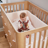Baby with pacifier in FLEXA baby bed, OAK, soft bedding and bumpers, nursery; child-safe rails visible.