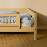 FLEXA SAND short safety rail from WHITE & NOR on toddler bed with blue-striped bedding in a beige children’s room.