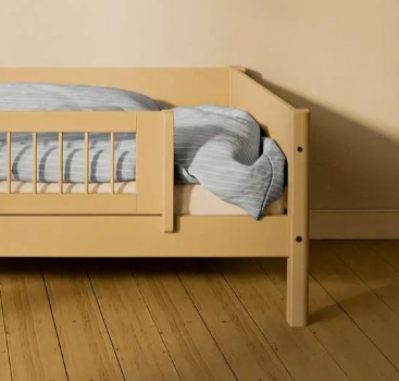 FLEXA SAND kort sikkerhedsgelænder fra WHITE & NOR på en børneseng med blåstribet sengetøj i et beige børneværelse.